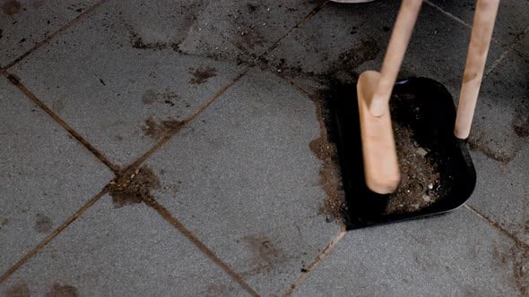 Static close up sweeping up dirt in a dust pan from a dirty tiled ...