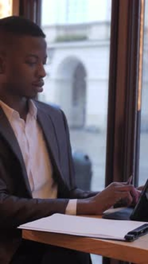 African Businessman Taking Notes and Using Tablet at Cafe