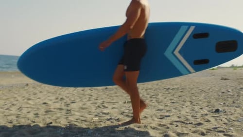 Man Walks on the Beach with Stand Up Paddle