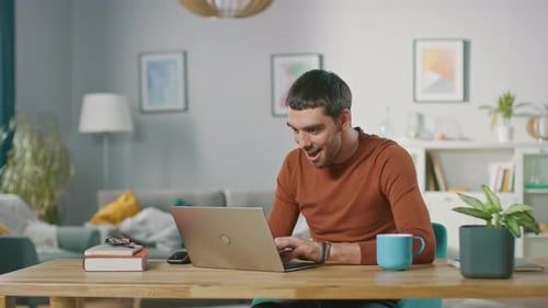 Excited man uses laptop in bright living room