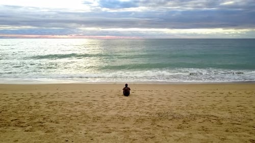 Einsamer Typ, der beobachtet, wie die Wellen am Ufer brechen, sitzt alleine am Strand