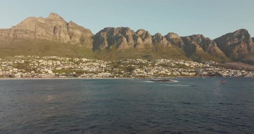 Drohne fliegt hoch rückwärts über das hügelige Meer am Strand von Camps Bay in Kapstadt, Südafrika - ma
