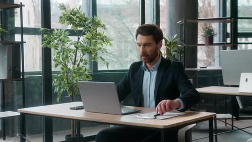 Concentrated Caucasian Businessman Typing Laptop in Modern Office Writing Notes Professional Male