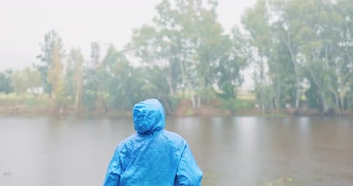 Person in Raincoat Celebrates Near Lake