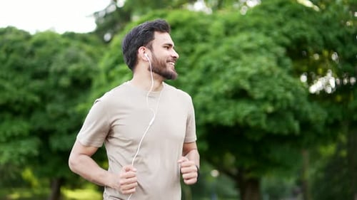 Young adult male runner jogging in urban city park. Handsome active man with headphones enjoys joggi