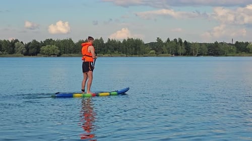 A Man in a Life Jacket on a Paddle Board in the Middle of a Lake Sports Lifestyle on the Lake