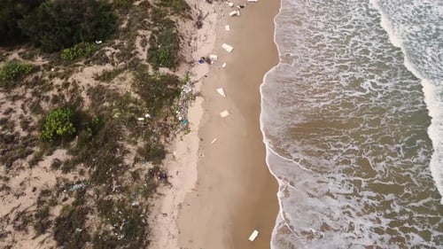 Aerial flyover polluted beach with foam board trash. Foamy tide waves rolling in