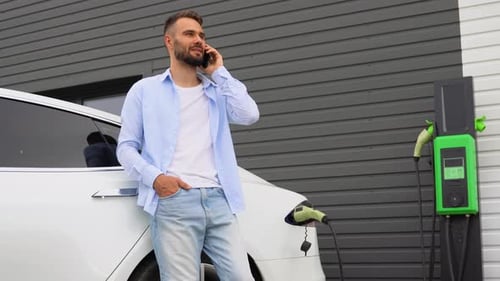A Man Talking on the Phone While Charging Luxury Electric Car at Charging Station