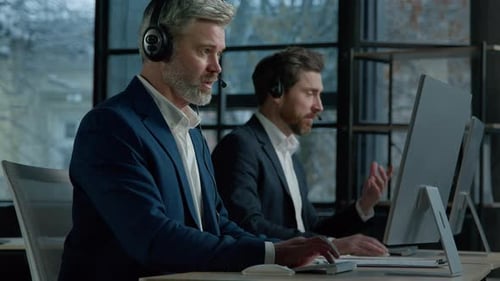 Two Men Call Center Service Operators Work in Office Talk to Client Using Headset on Computer