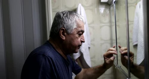 Stressed old man in front of bathroom mirror. Middle-age crisis