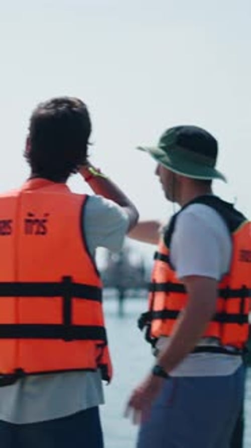Two Young Men in Life Jackets Discussing Kayaking Routes on a Lakeside Pier