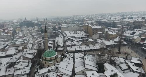 A cinematic drone aerial view of Sarajevo’s Old Town, gently blanketed in fresh snow.