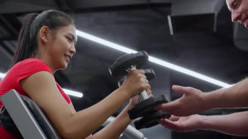 Woman Lifting Weights with Trainer in Gym