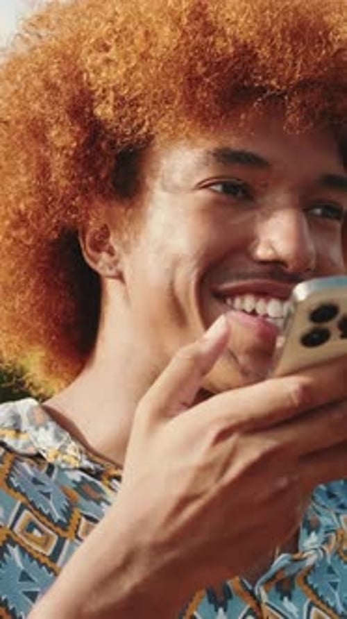 Close-up of young guy sitting on bench, chating online with smartphone in his hands and smiling