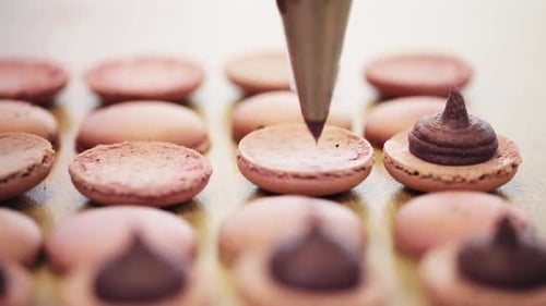 Chocolate Filling Being Added to Light Brown Macarons