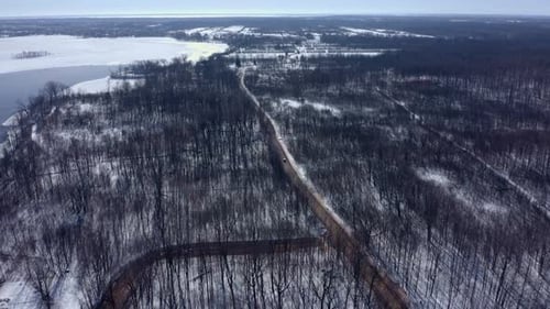 Aerial shot moving forward over a forest in winter following a car on the road