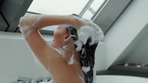 Woman washing her dark hair with shampoo in bathroom