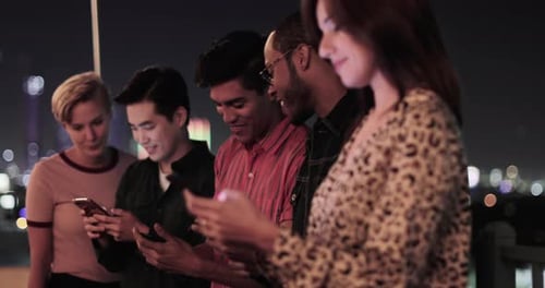Group of friends on smartphones outdoors in city at night