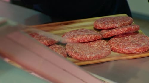 Raw meat burger patty with salt, pepper and rosemary on wooden cutting board.