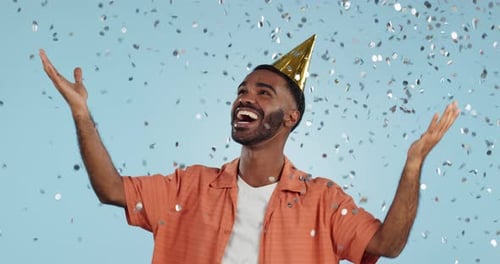 Man, birthday party hat and confetti in studio, smile or surprise for celebration by blue