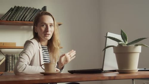 Une jolie femme parle assise à une table devant un ordinateur portable et gescule activement avec