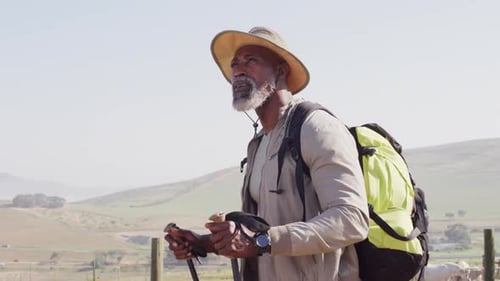 Senior african american man hiking with trekking poles on sunny day, slow motion