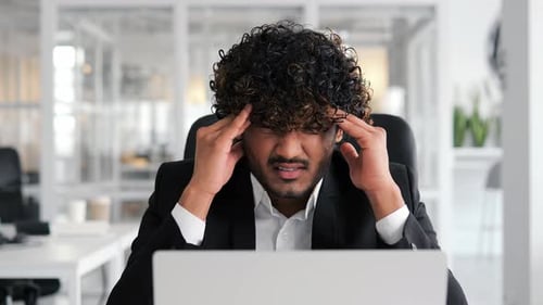 Young Indian Man in Office Experiencing Severe Headache at Workplace
