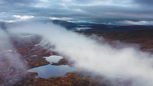 Heavy gray clouds hang above the autumn valley. The fog creeps in the lowland and rises. A narrow ro