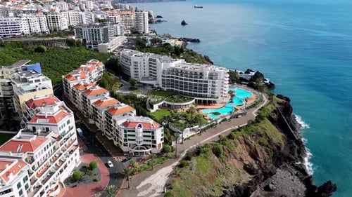 slow drone shot of coastal hotels in madeira , with blue sky and blue sea with stunning white buildi