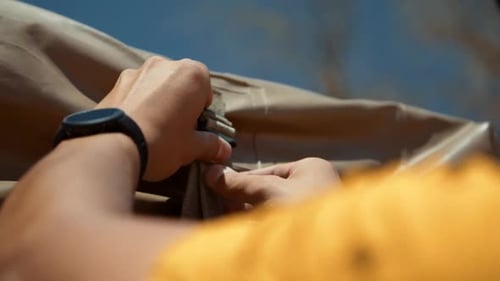 Plan rapproché des mains d'un touriste qui desserre les sangles de sa tente de toit en toile.