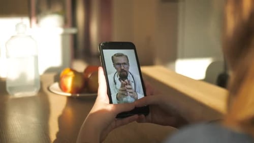 Back View Redhead Girl Holding Smartphone Looking at Screen Consulting Young Doctor Online Video