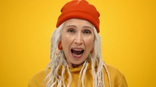 Excited senior woman cheering with fist raised on yellow