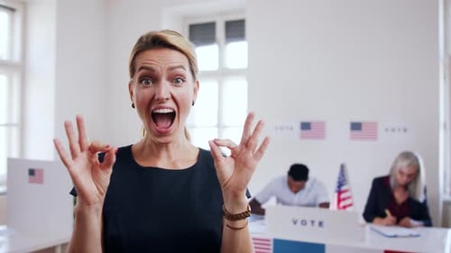 Happy young woman voter gives ok gesture at polling place USA elections