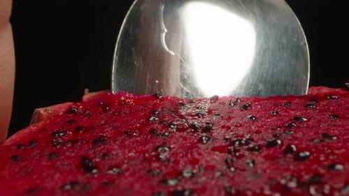 I scoop out the red pulp from the pitahaya with a spoon. Dolly slider, extreme close-up.