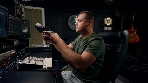 a focused male sound engineer wearing headphones sits at a mixing desk recording new track