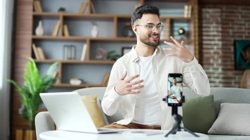 Man Presents into Phone on Table with Laptop