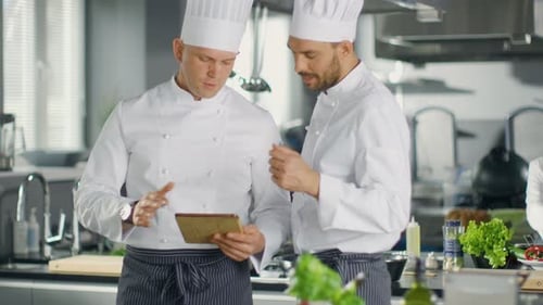 Two Famous Chefs Exchange Ideas About Video Blog Recipe they Watching on Tablet. They are Working i