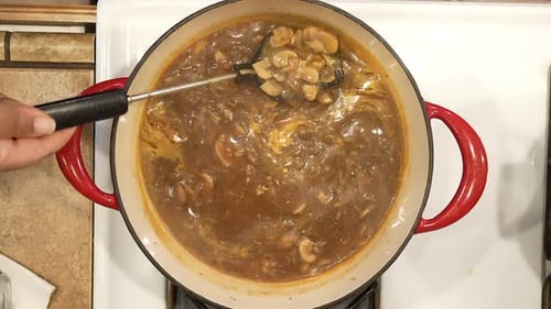 Stirring vegan wild rice and mushroom soup as it boils on the stove - overhead view in slow motion W