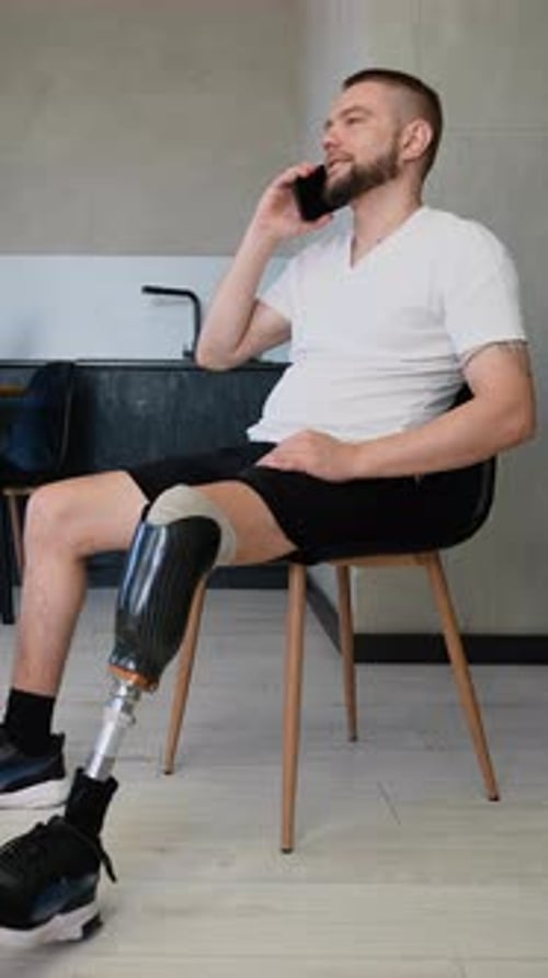 A Man with a Prosthetic Leg Sits Comfortably in His Stylish Apartment Smiling While Talking on the