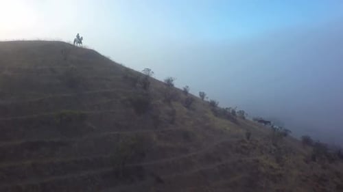 Lone Horseman Rides on Hillside in Misty Landscape