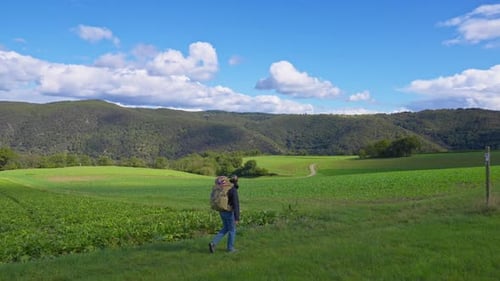 One person walking with large backpack on a green meadow while surrounded by panoramic nature views