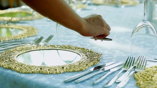 The woman is preparing the table for the event in the garden. hand putting a fork and knife on the t