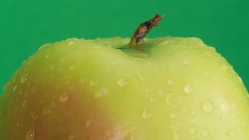 Saftiger grüner Apfel in Regentropfen, die sich auf grünem Hintergrund drehen