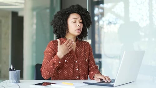 Young african american female employee is hot sitting at the workplace in office. Black woman waves