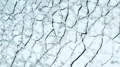 Aerial fly over view of cracked ice floes floating in the sea. Large densely dispersed pieces. Forwa