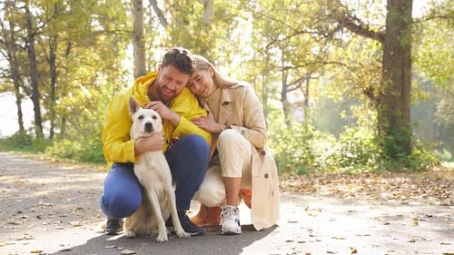 a Married Couple is Playing with a Kind White Domestic Dog in the Forest on a Sunny Autumn Day