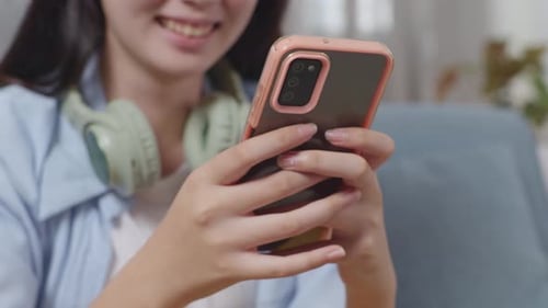 Close Up Of Asian Teen Girl'ຫ Hands Playing Smartphone While Sitting On Sofa In The Living Room