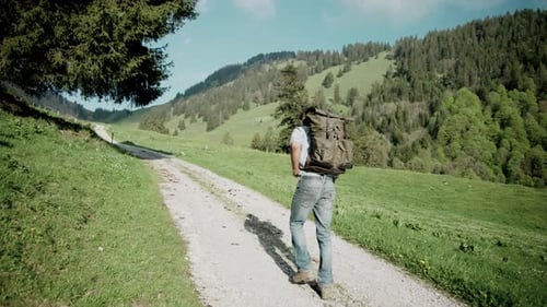 Backpacker millennial man hiking on rural countryside dirt path, slow motion