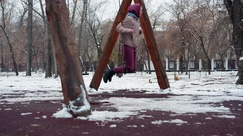 Lady Swinging in Winter Park with Snow and Trees in Background