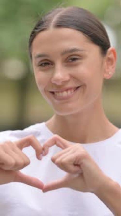 Smiling Woman Makes Heart Shape with Her Hands